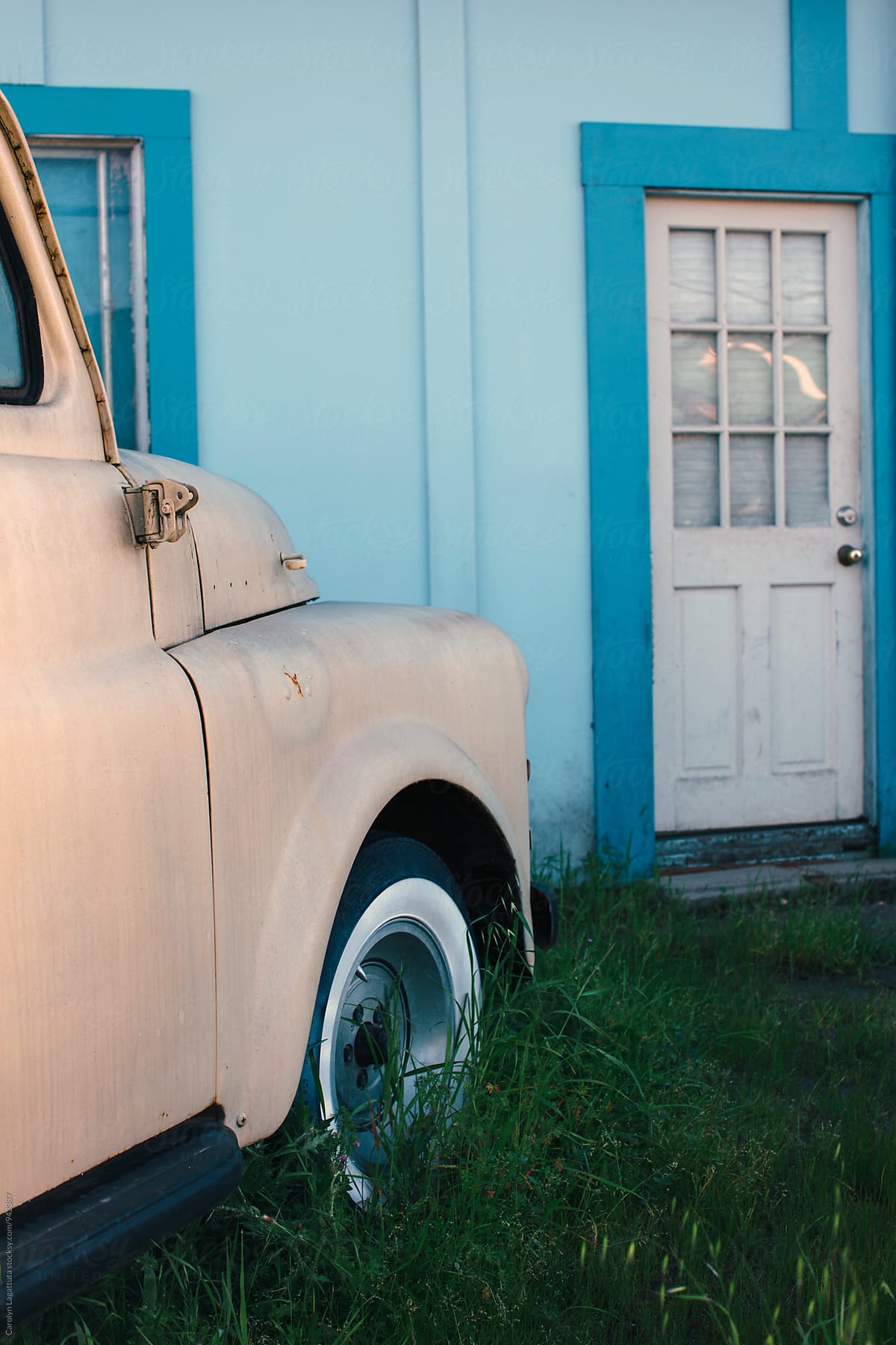Vintage truck parked in the tall grass in front of a blue house