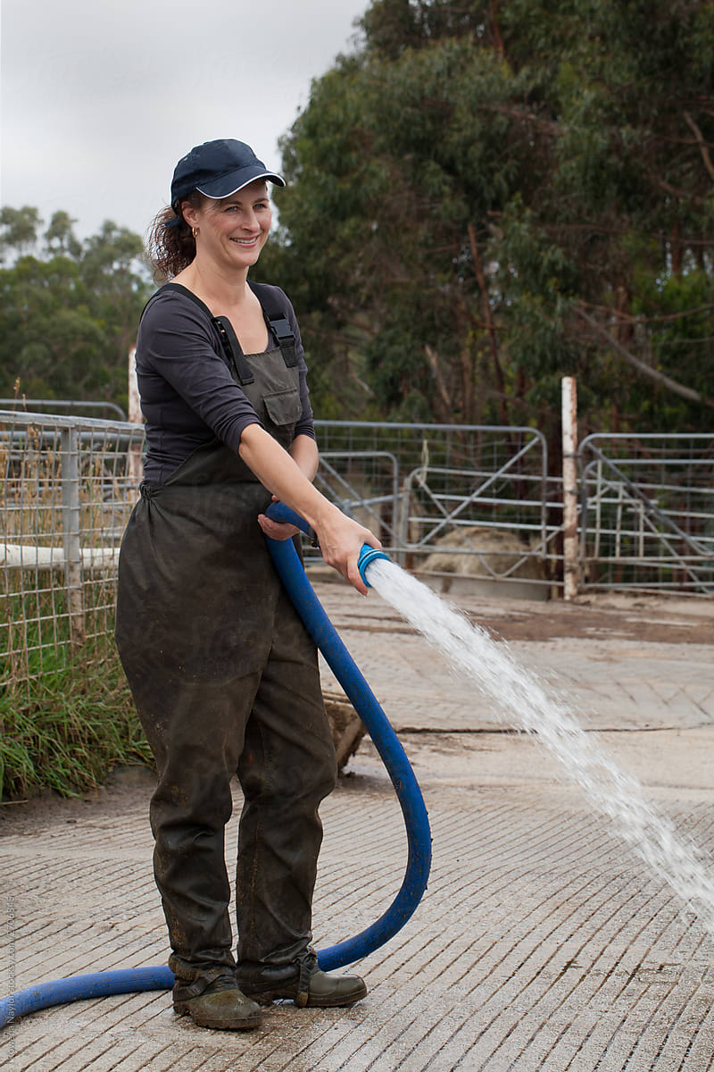 Female dairy farmer hosing down the dairy yard after milking