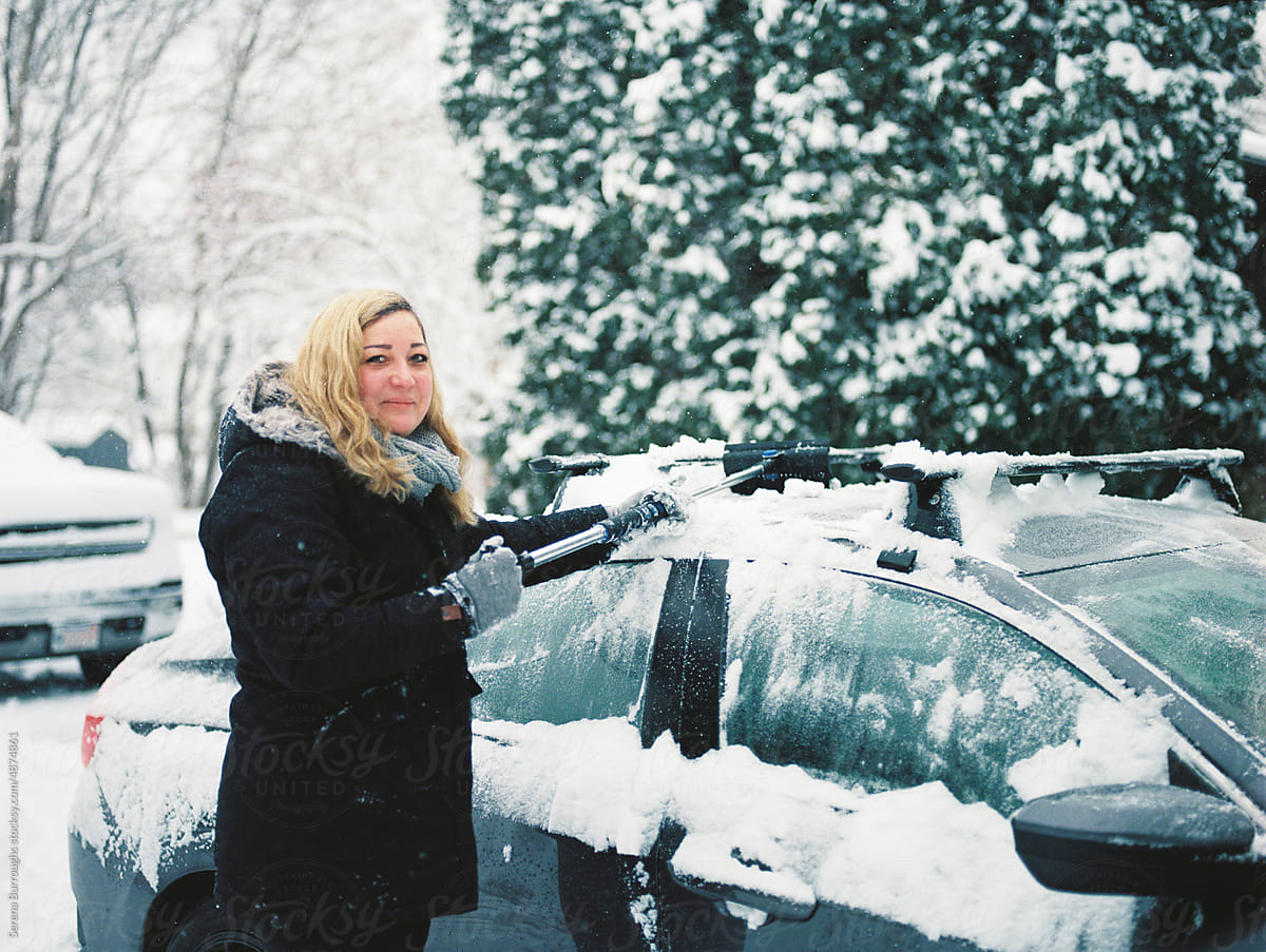 Woman clearing snow off her car in winter