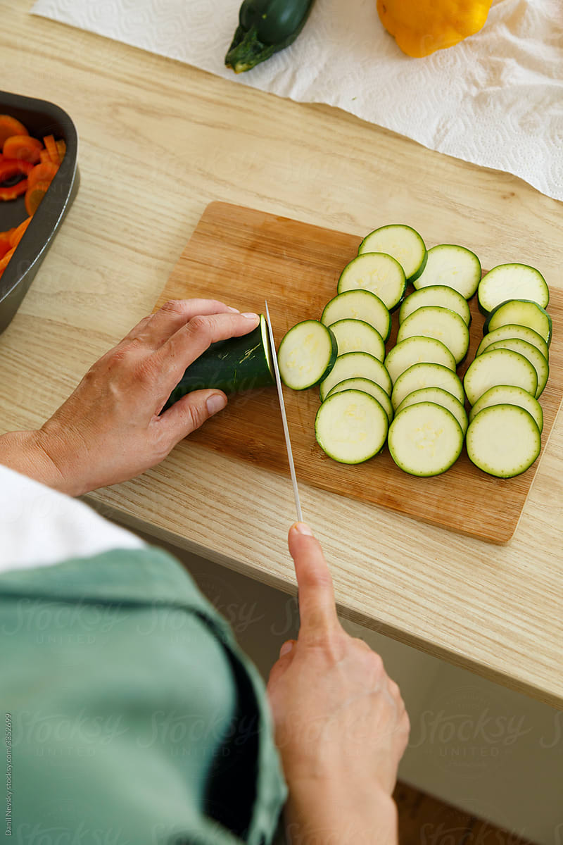 Crop housewife chopping zucchini in kitchen