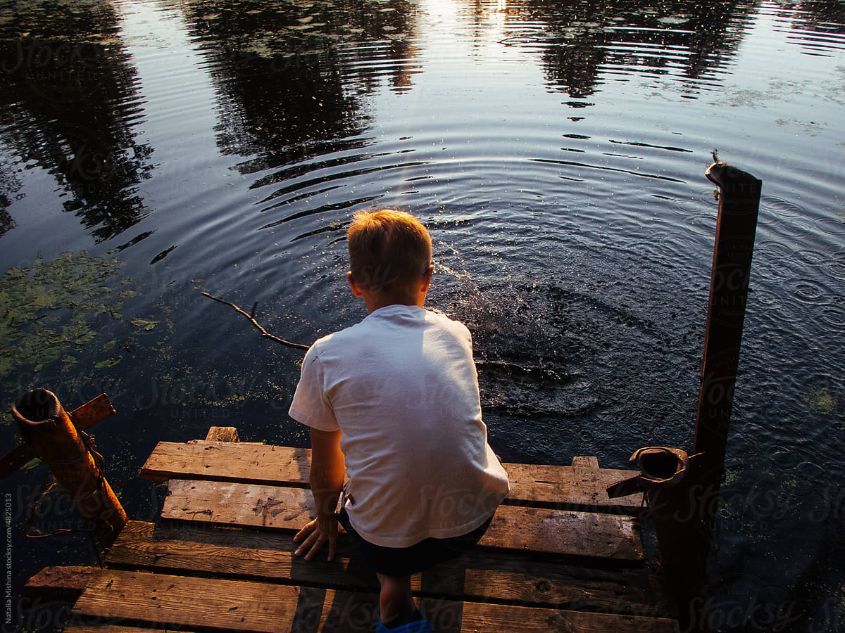 A boy on a wooden bridge drives a stick through the water.