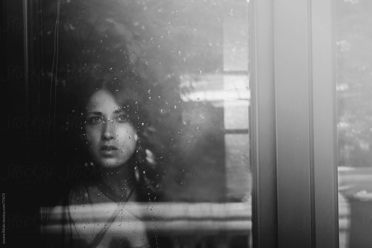 Beautiful girl standing at the window watching the rain