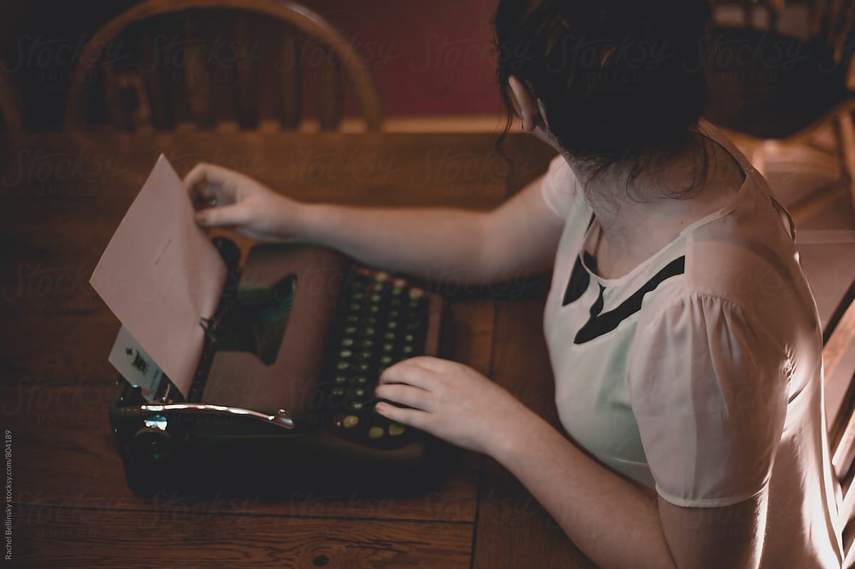 A young woman writes at an old fashioned typewriter