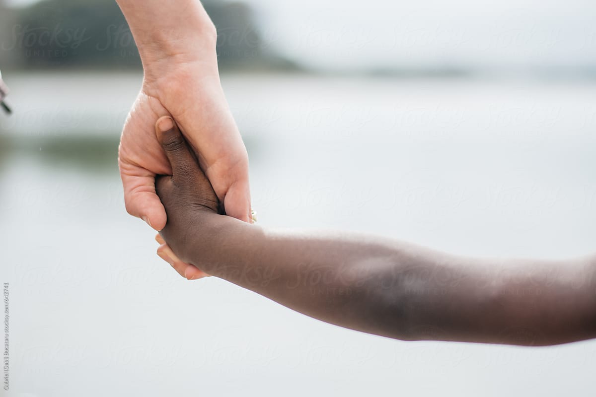 Caucasian woman\'s hand holding a black child\'s hand by a lake