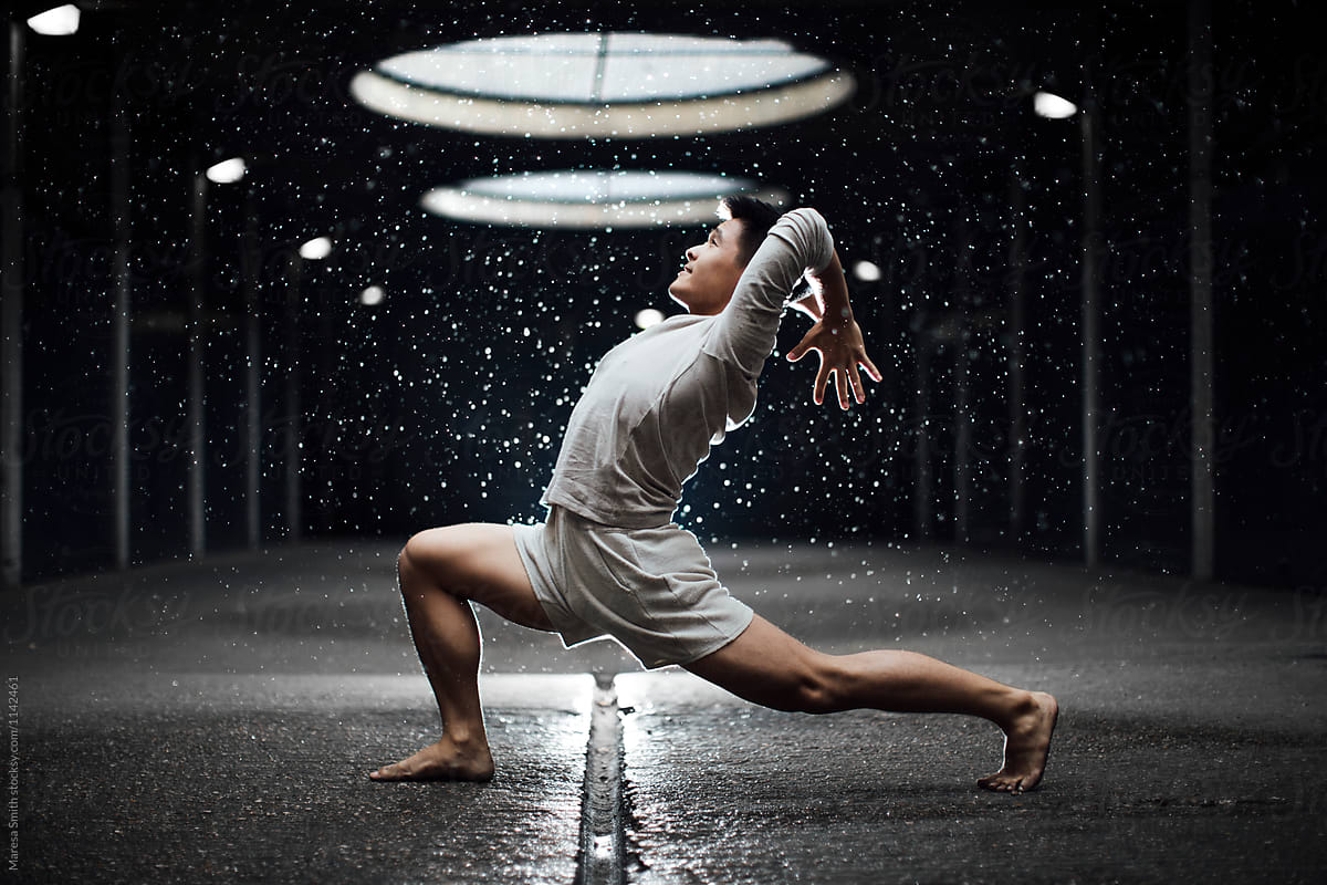 An asian man in an urban setting practising yoga in the rain