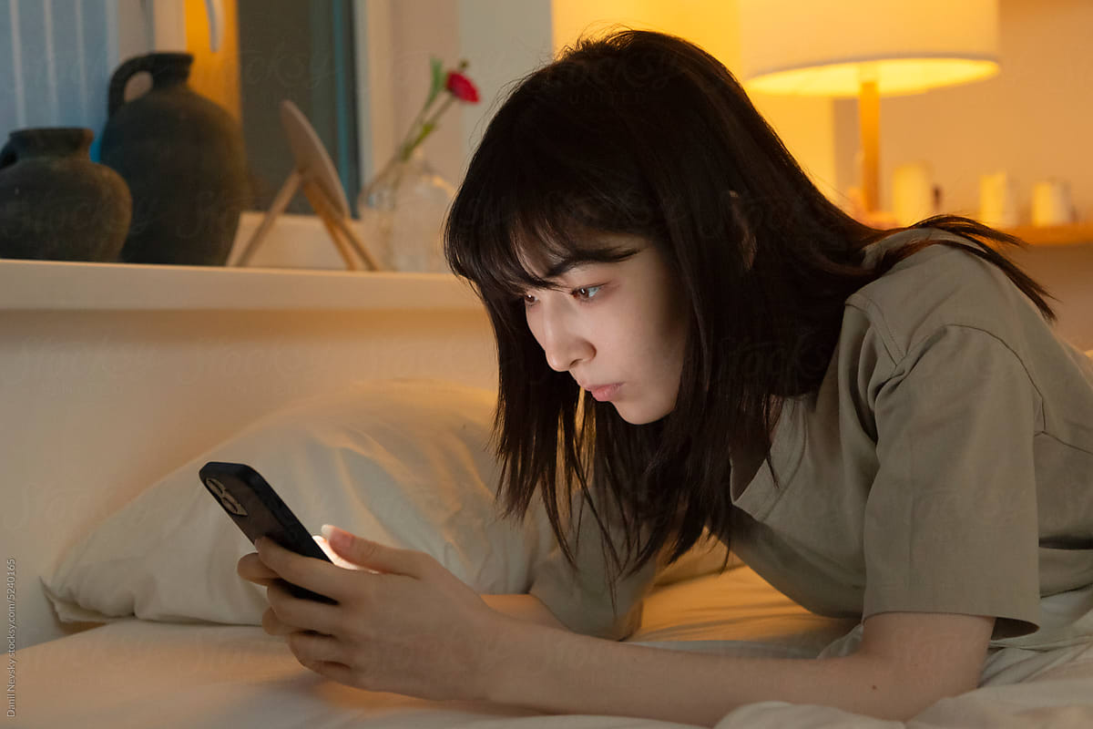 Focused Asian woman browsing mobile in bed