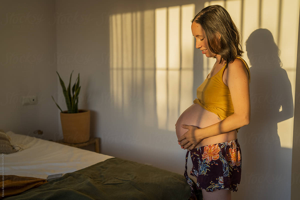 Expectant woman caressing her belly at home