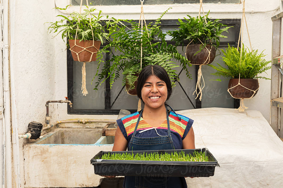 A smiling woman holding a tray of pea microgreens sprouts