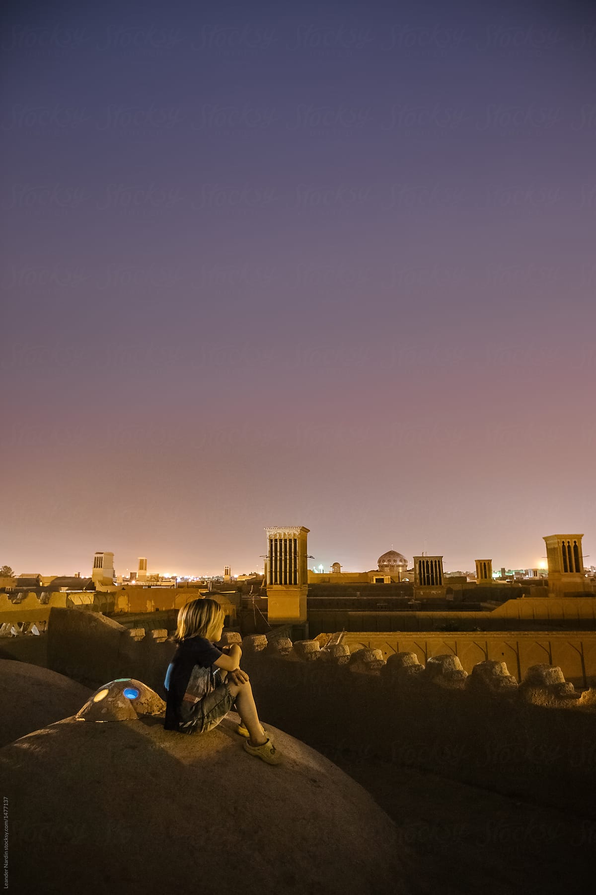 young boy sitting on roofs of the desert city yazd enjoying sunset, iran