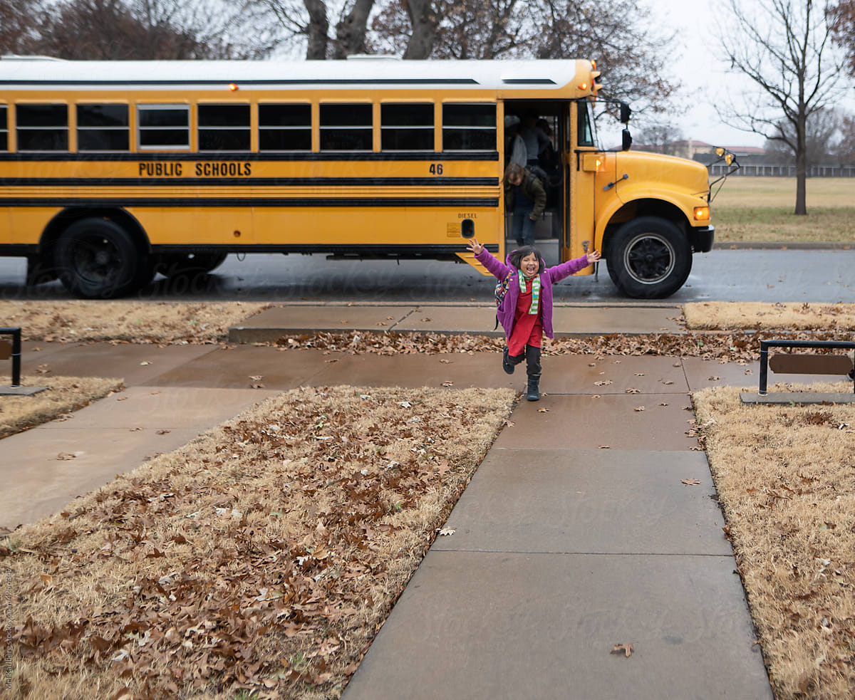 Girl running up sidewalk from school bus
