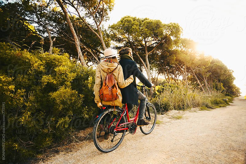 Back view of a hipster couple riding a bicycle in the forest.