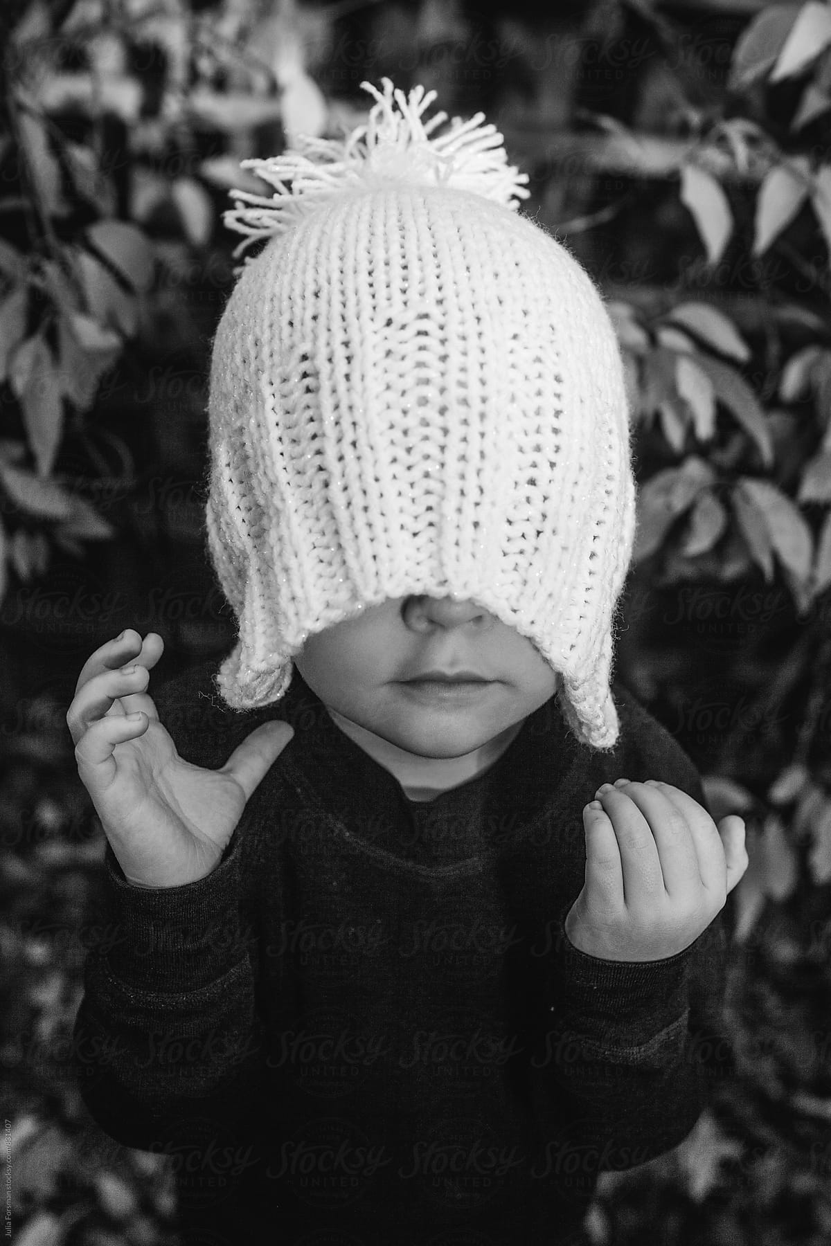 Little girl pulls a woolly hat over her eyes.