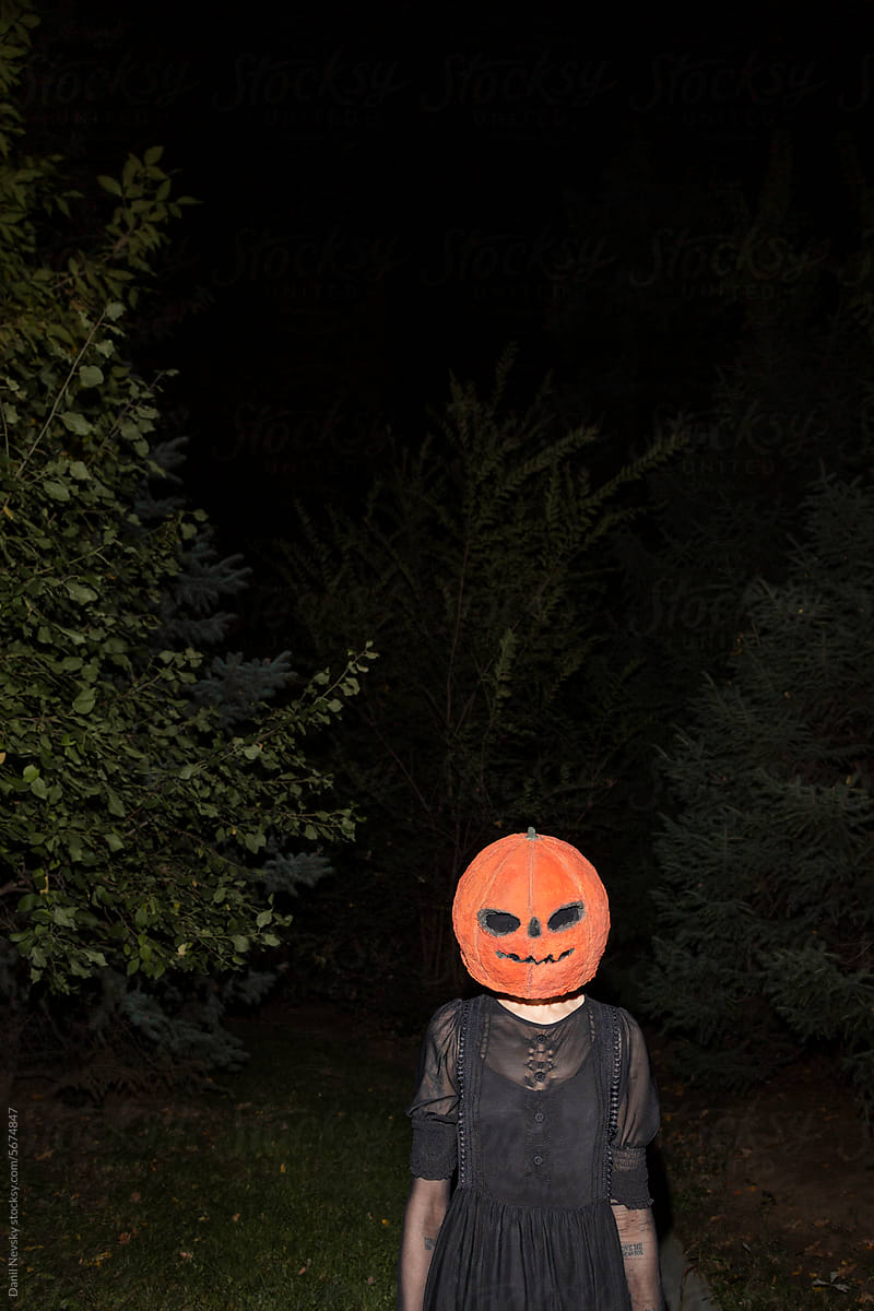 Woman with pumpkin on head standing in dark park