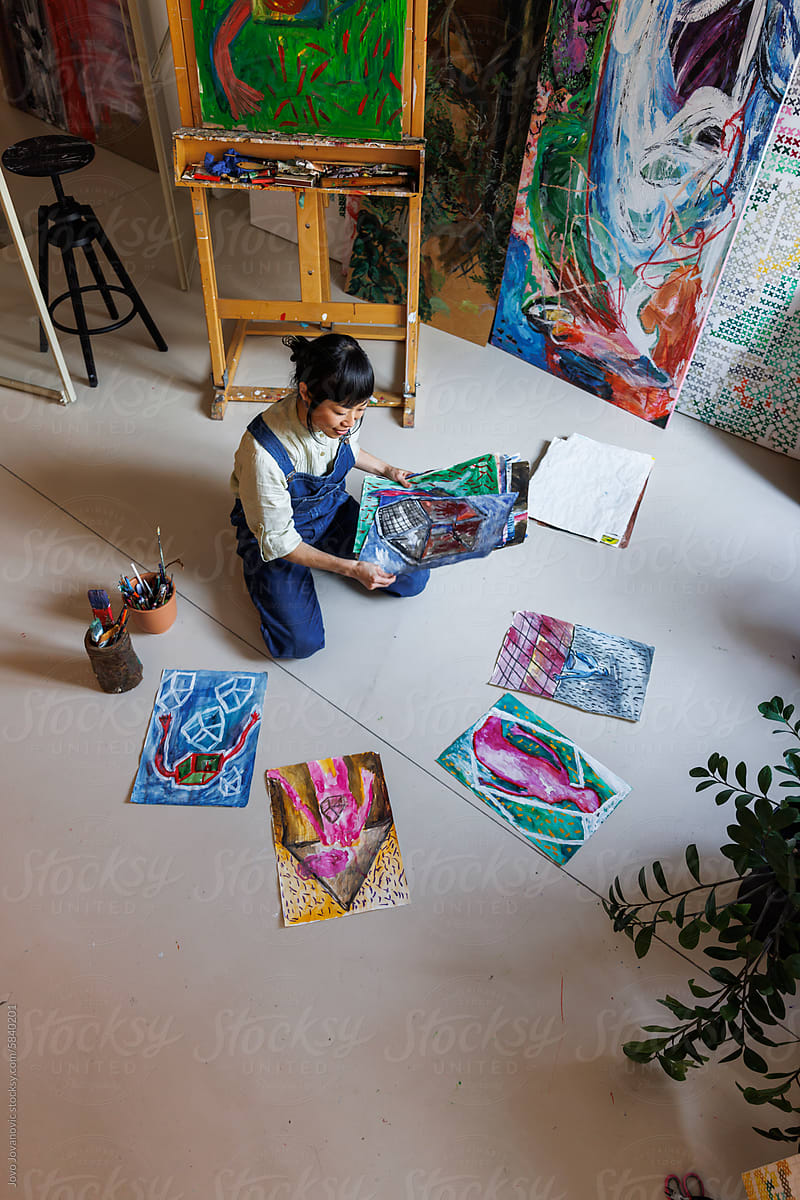 High angle view of artist arranging various paintings on floor