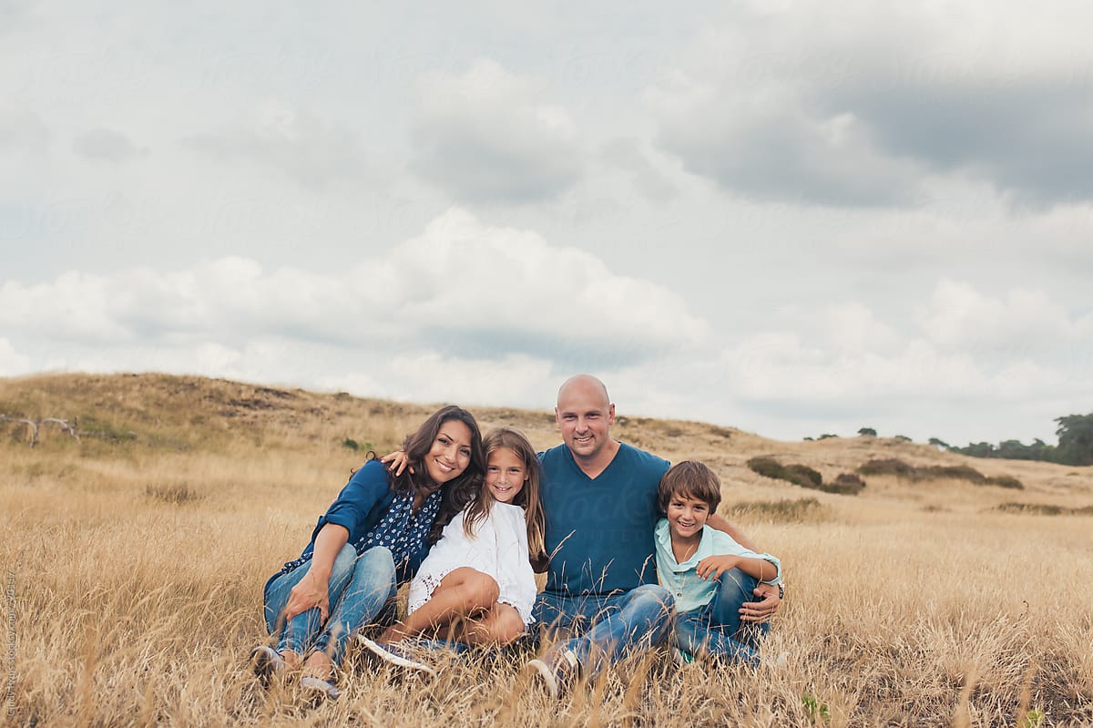 Family of four sitting in a golden field underneath a big cloudy sky