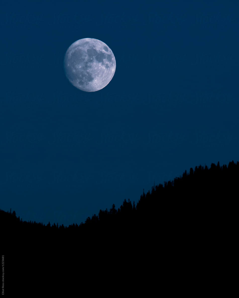 A full moon rises over a mountain
