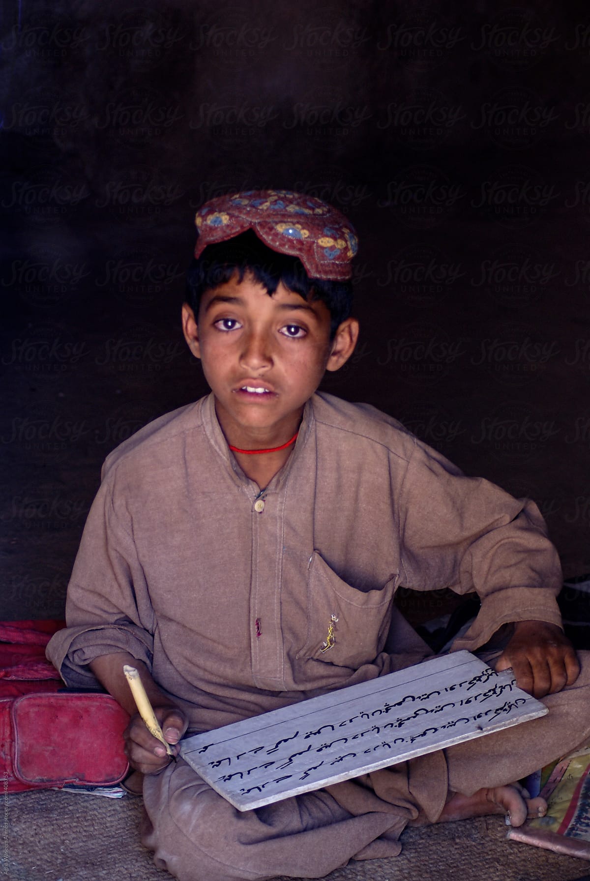 An Adolescent Afghan School Boy Learning to  Write on a wooden Tablet