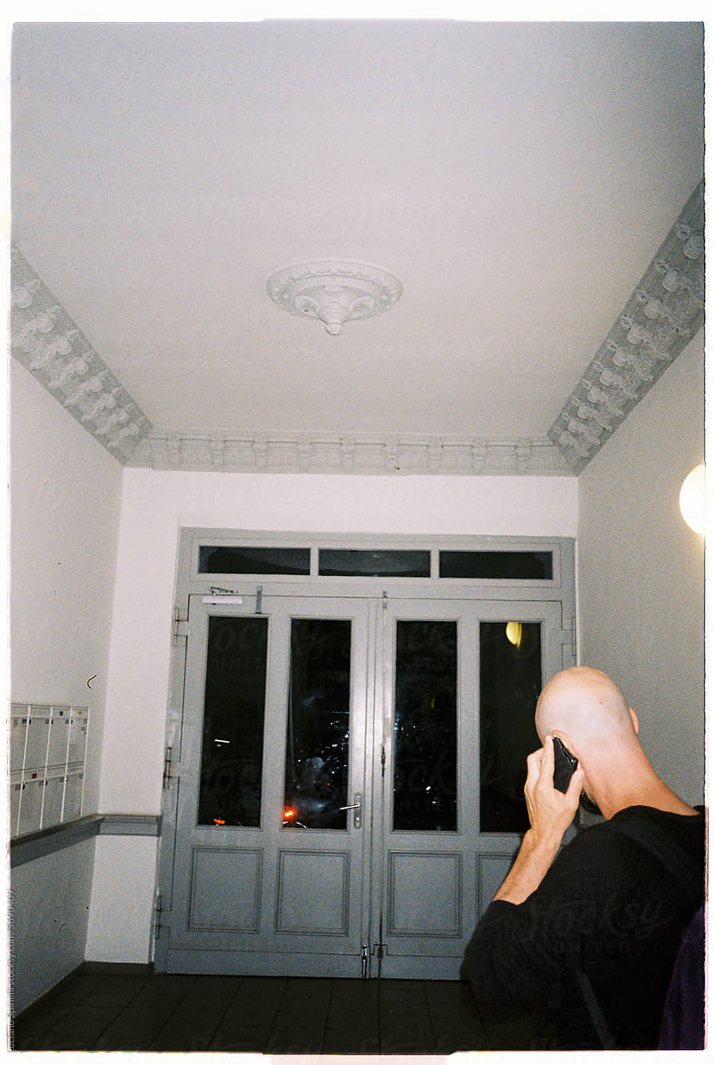 Bald man talking on the phone in front of large gray door inside hall