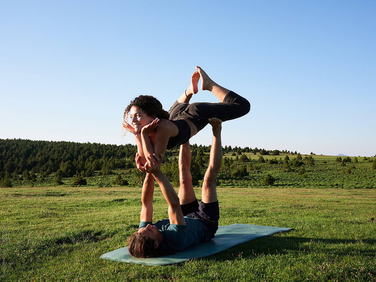 Couple balancing in acro yoga pose on field grass