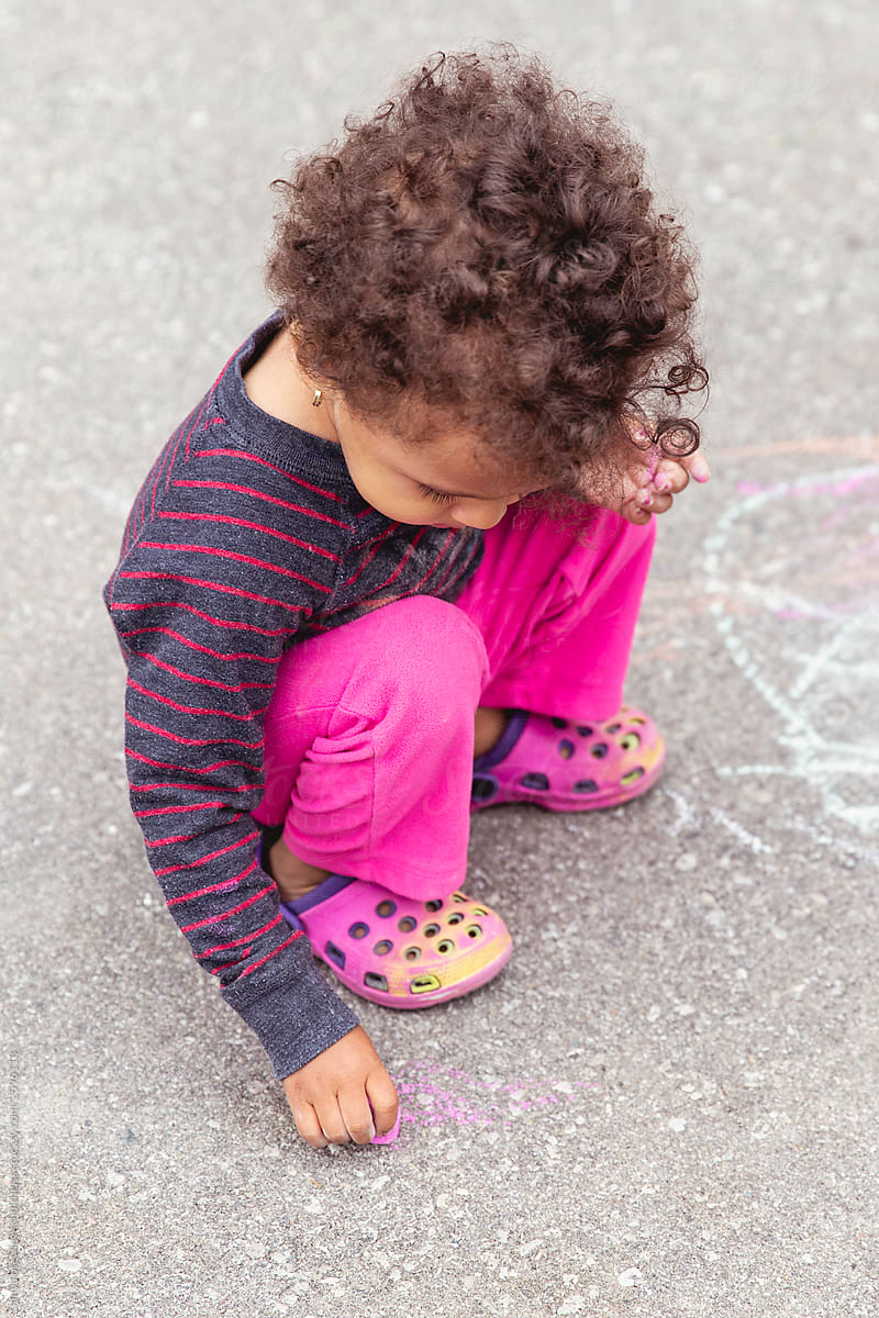 Cute toddler child drawing with a large piece of chalk