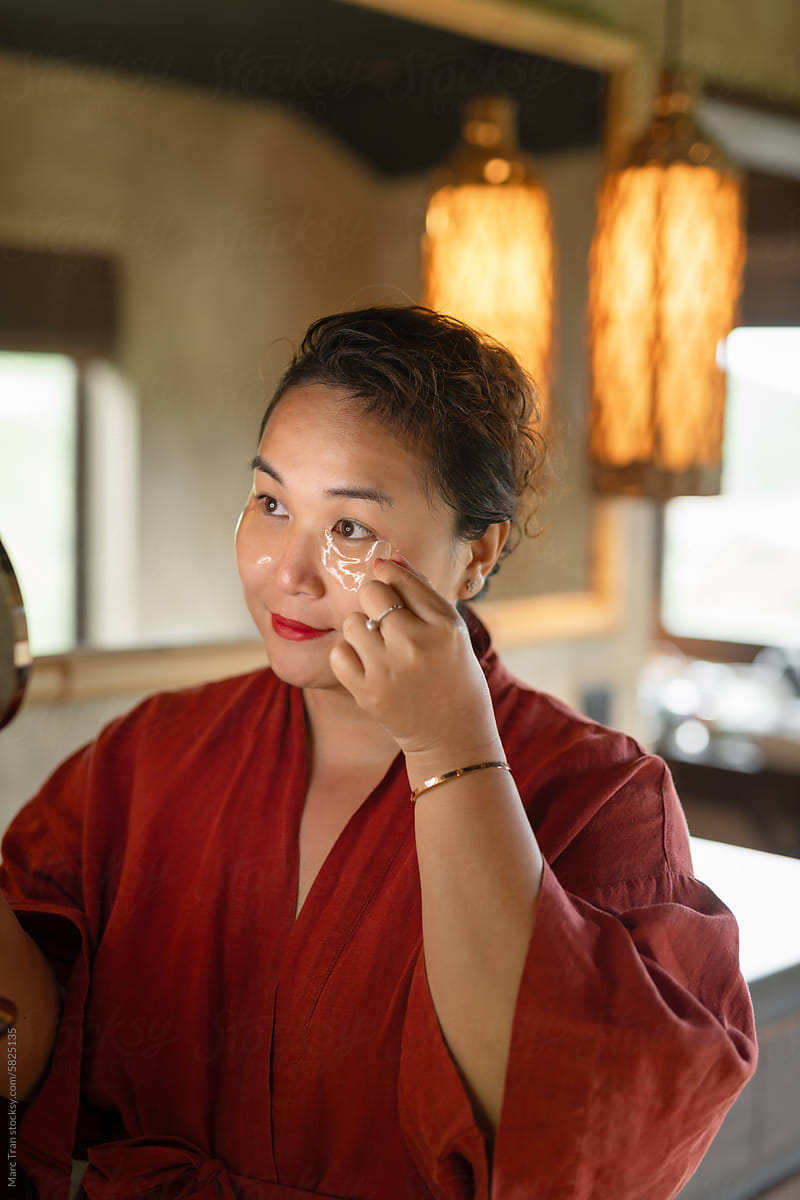 Plussize asian lady holding mirror and applying under eye