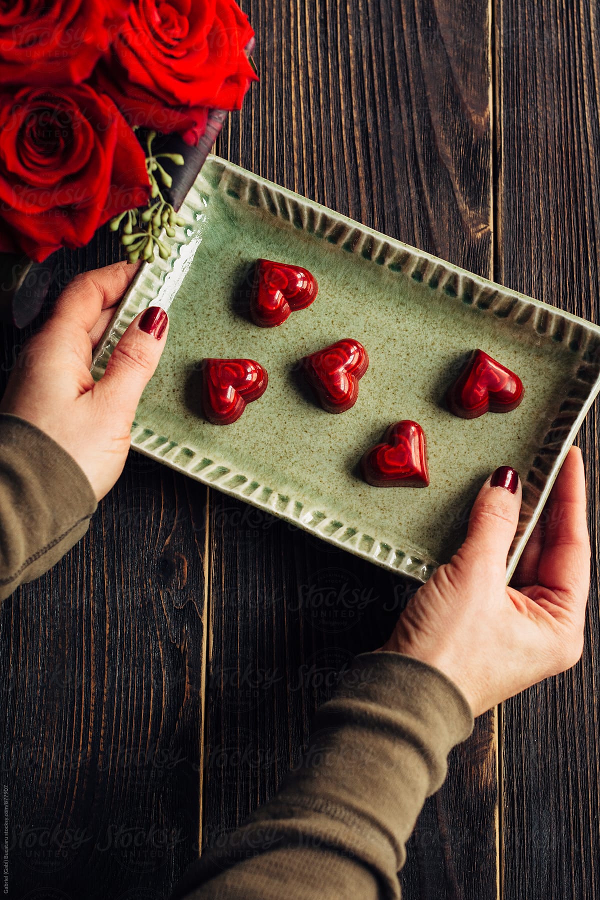 Woman\'s hands holding a tray with red heart shaped chocolates