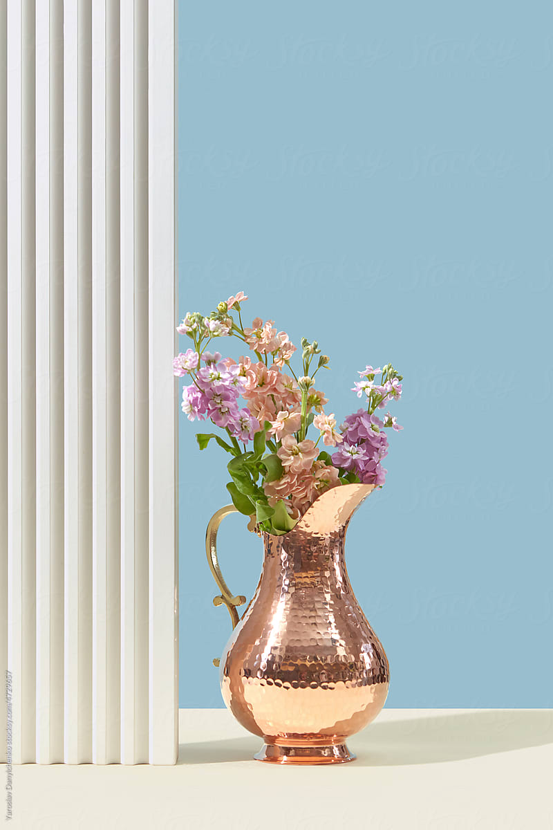 Shiny elegant copper jug with fresh flowers .
