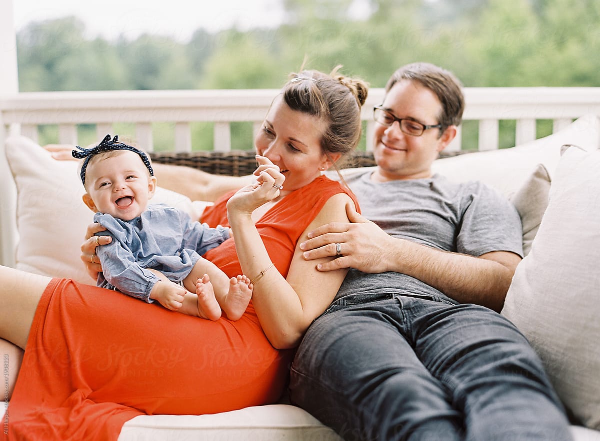 Mom And Dad Snuggling While Young Daughter Laughs On Porch By Stocksy Contributor Ali Harper 