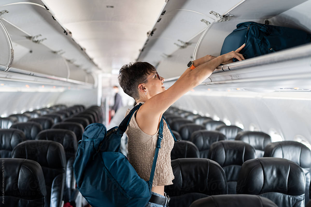 Woman placing luggage in overhead bin.