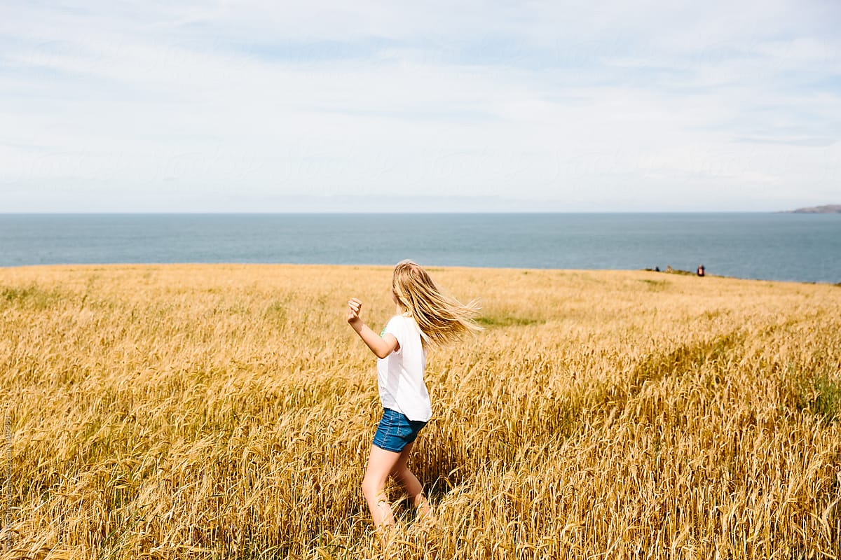 Little girl running through a field of ripe wheat with the sea in the background