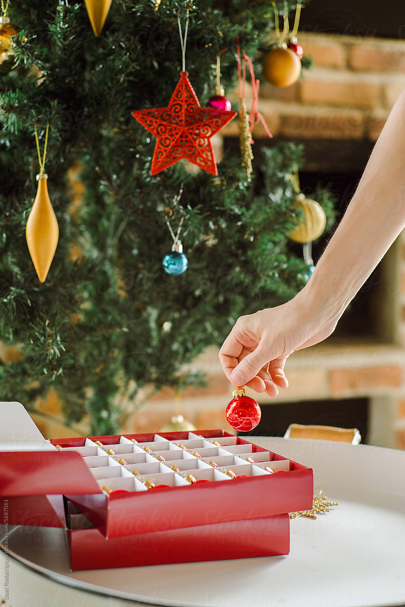 A woman's hand pulls a Christmas ball out of a box