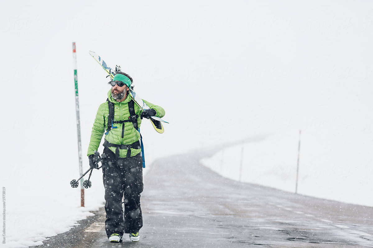 Skier walking along empty road in the snowy mountains in winter carrying skis
