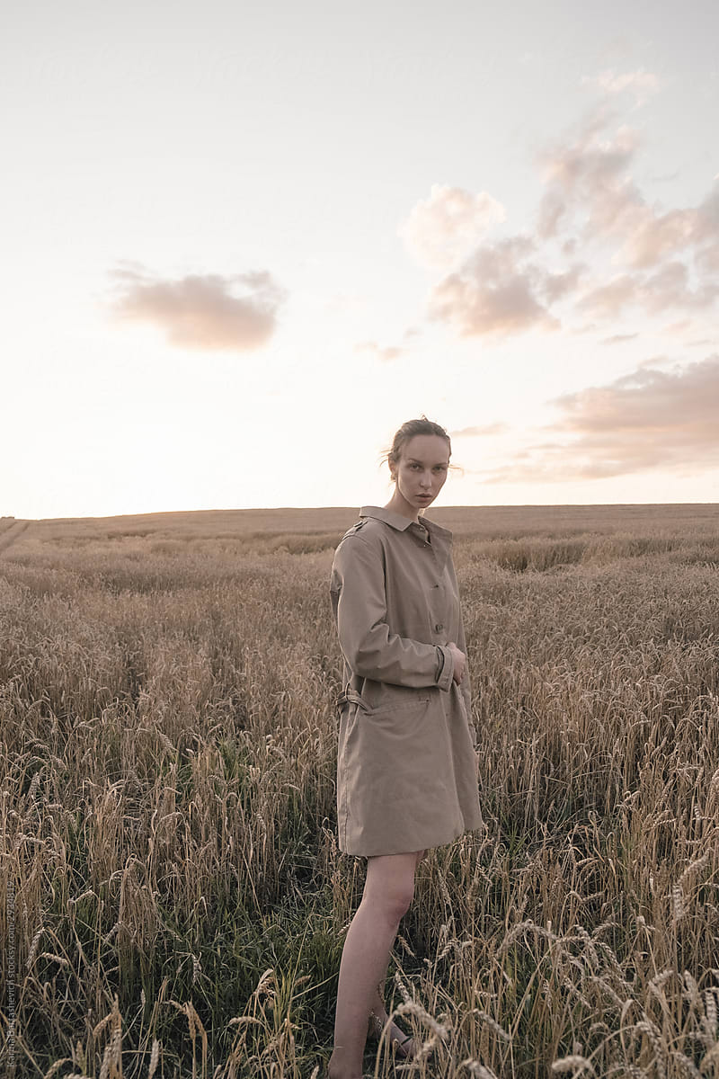 blonde girl with gathered hair in a beige coat on a walk along a wheat field