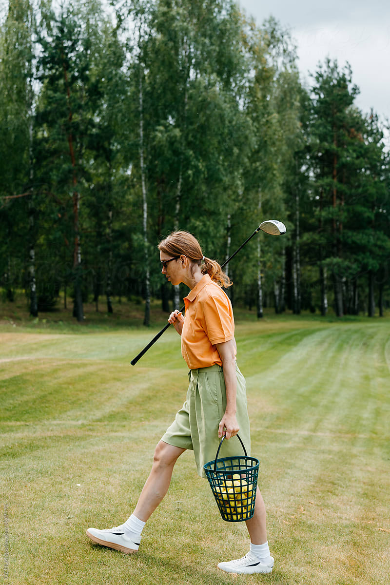 A woman with golf equipment in her hands walks across the golf course