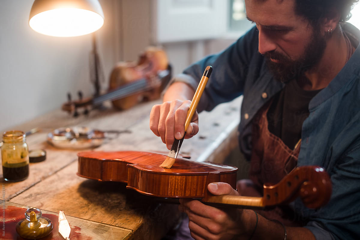 Young luthier restoring and varnishing an old violin