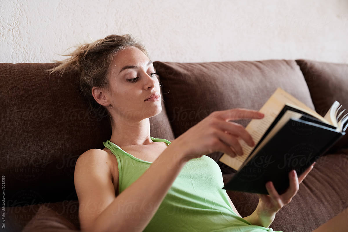 woman in green top reading book on sofa.