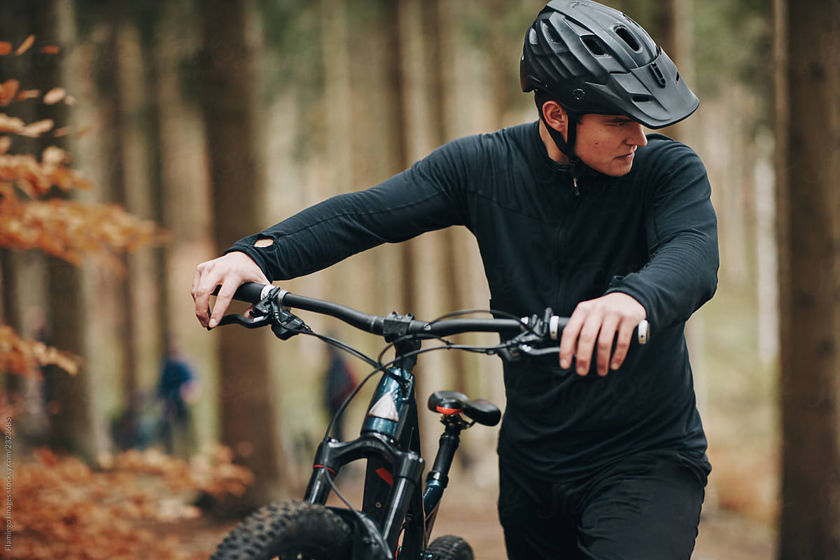 Young man pushing his mountain bike up a forest trail