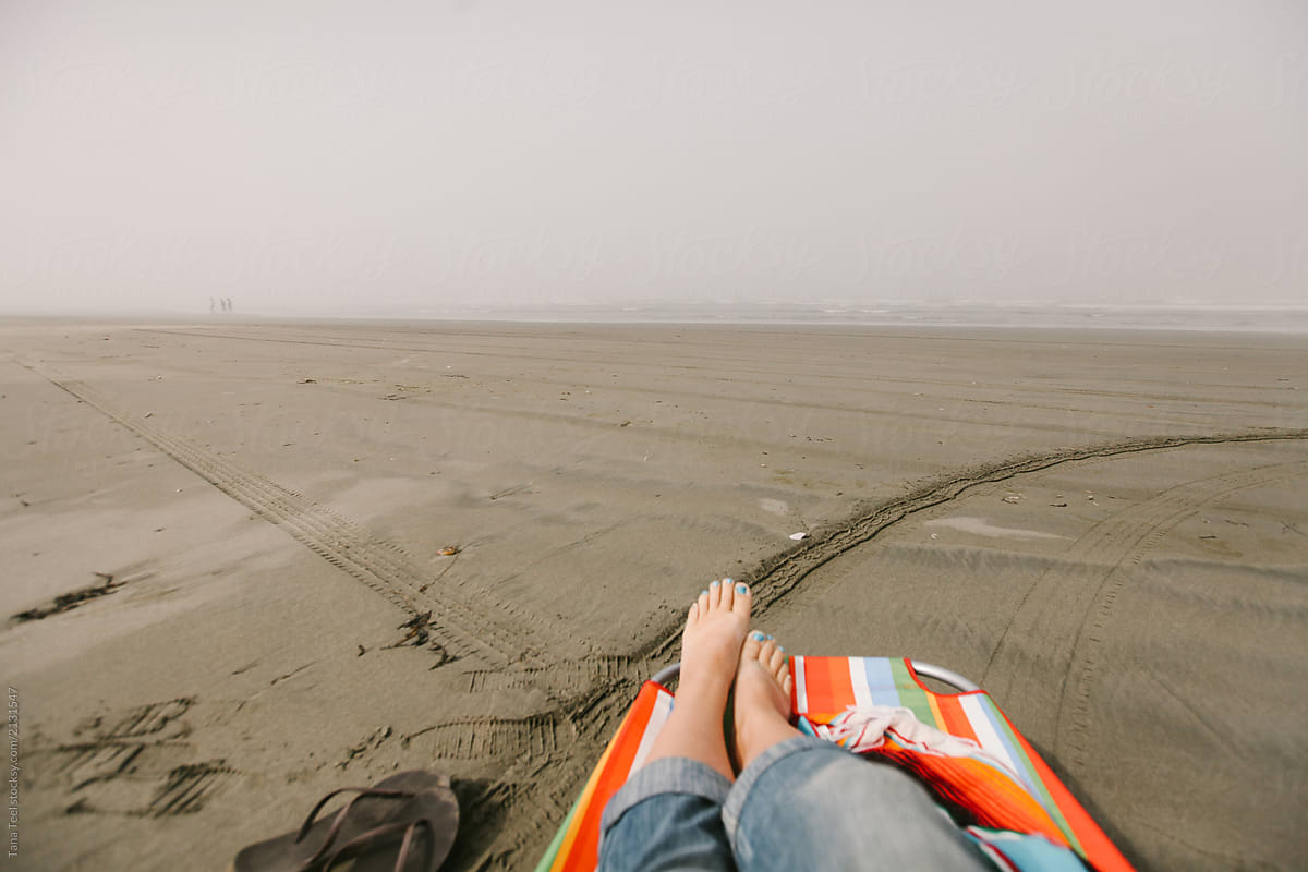woman relaxes barefoot in lounge chair on beach on misty morning
