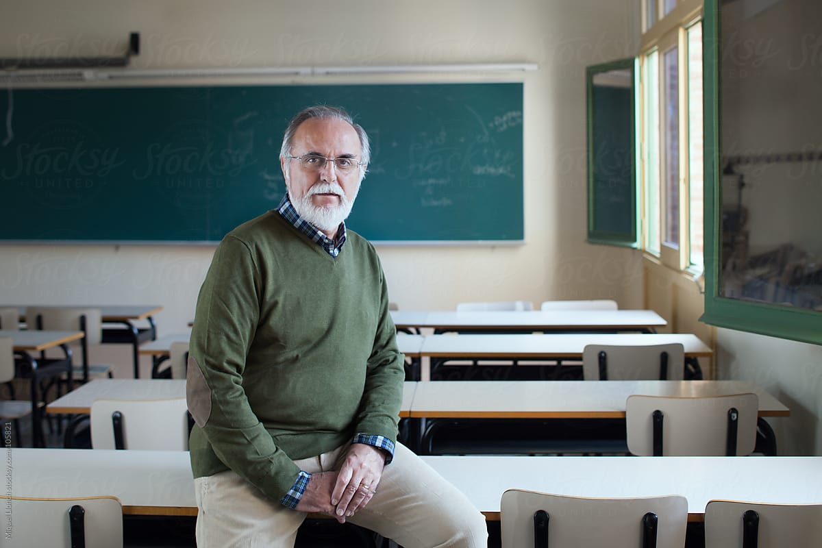 Portrait of a bearded senior professor sitting on a classroom desk