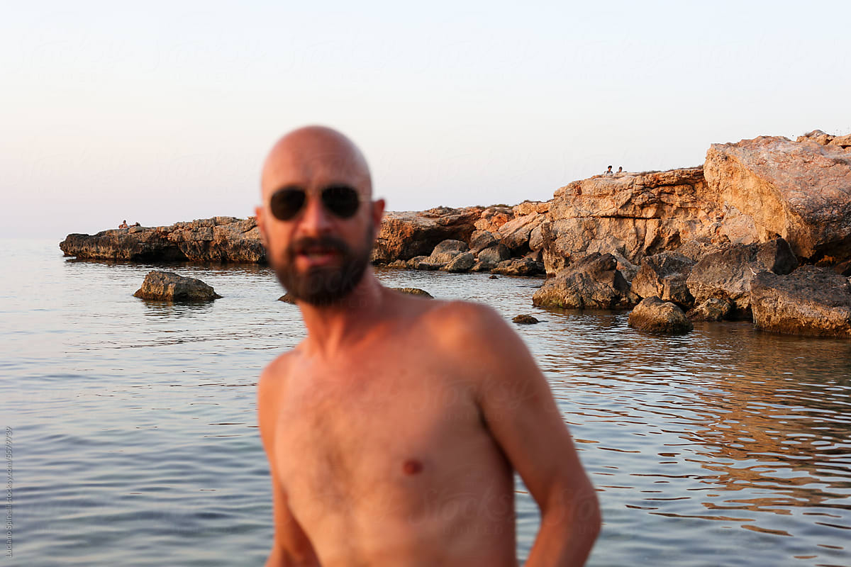 Portrait bold shirtless man with sunglasses at the beach eye contact