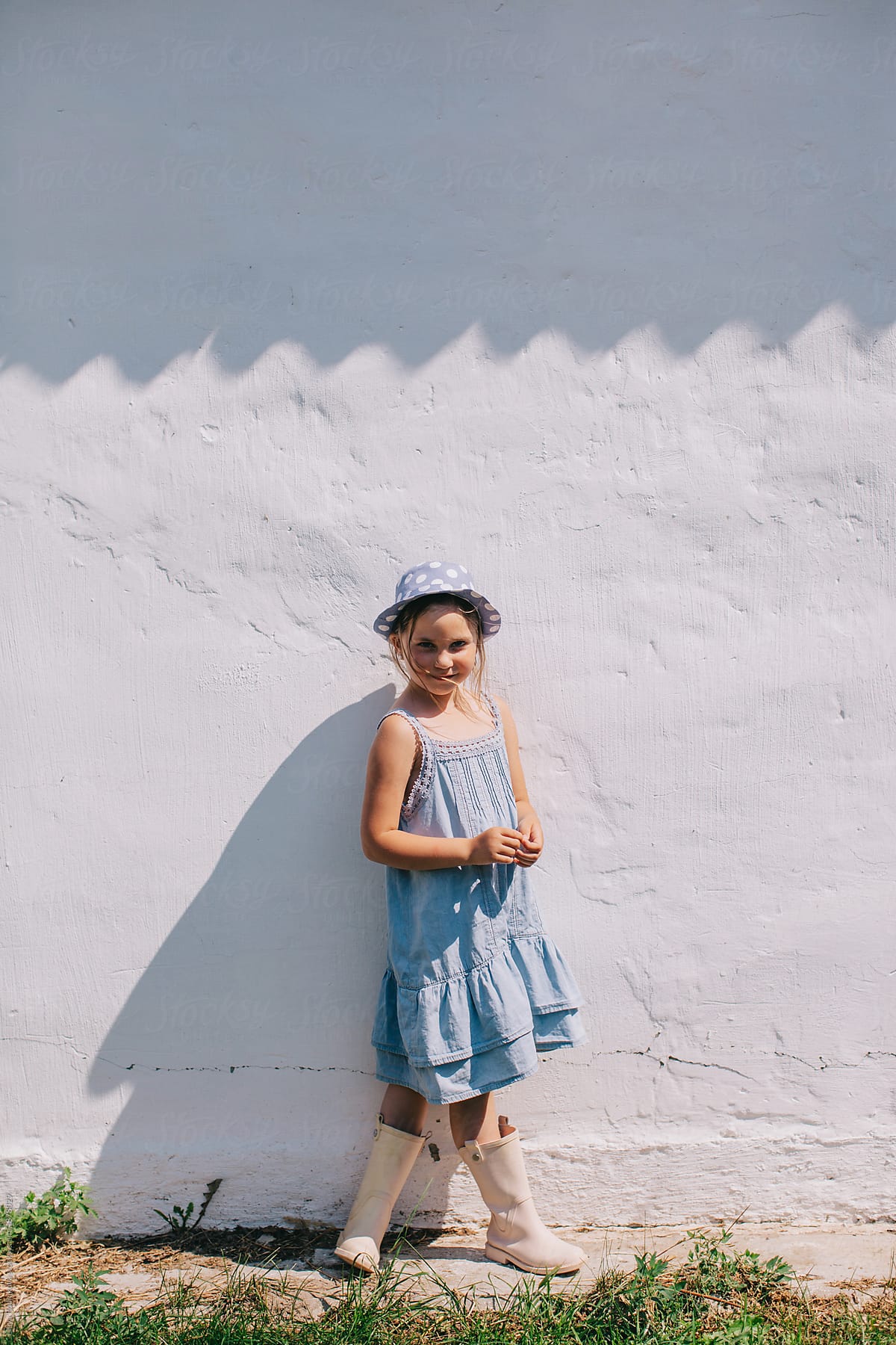 Stylish little girl posing by the white wall outdoors