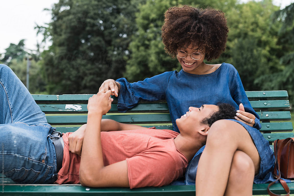 Happy young black couple sitting on the bench at the park