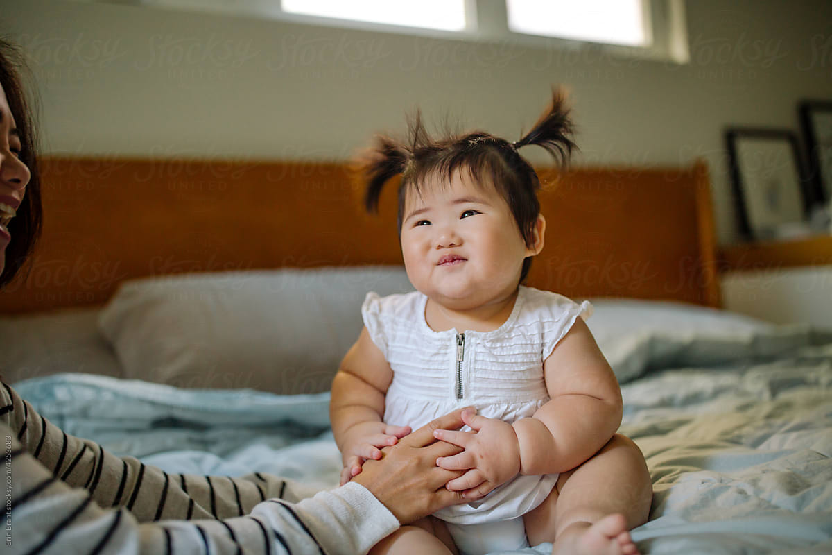 Smiling Asian baby with pigtails  on bed