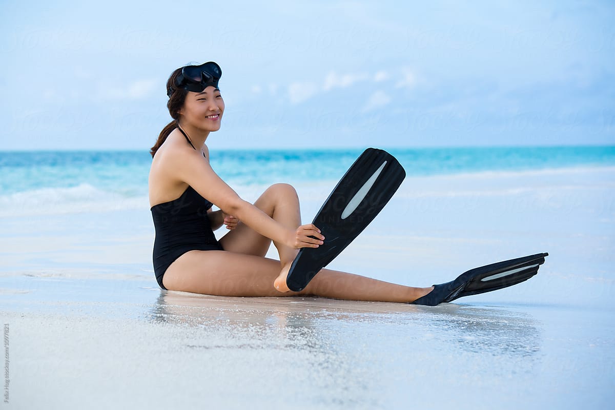 An Asian woman putting on fins
