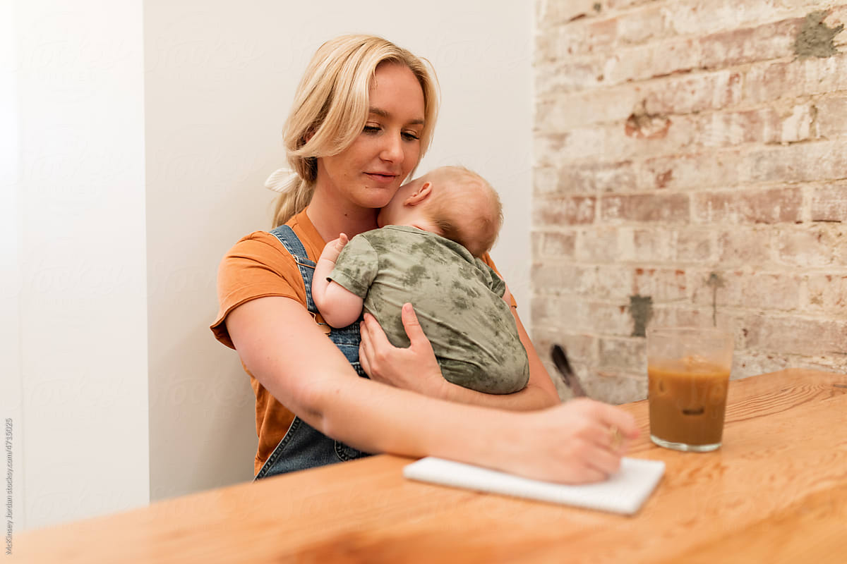 Young Mother Writes On Paper While Holding Son In Arms