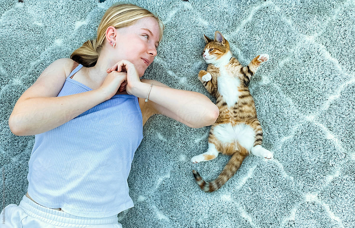 Teenage girl and her kitten chilling on a rug.