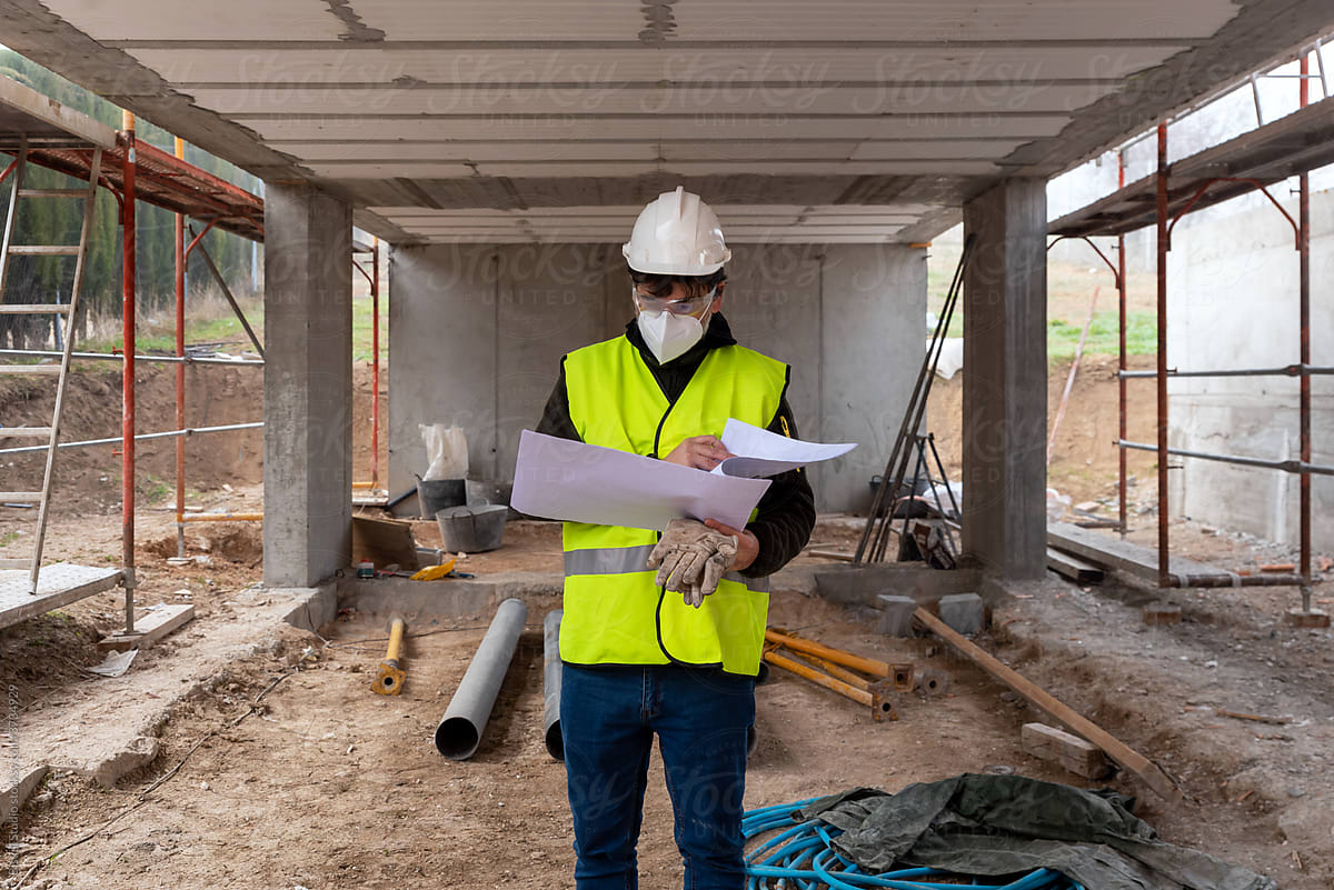 Construction engineer in protective mask examining blueprints