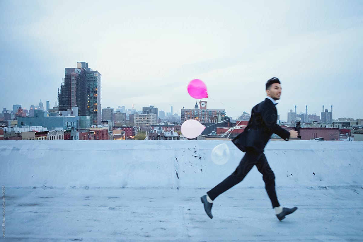Excited Young Man Running with Balloons on Rooftop in New York