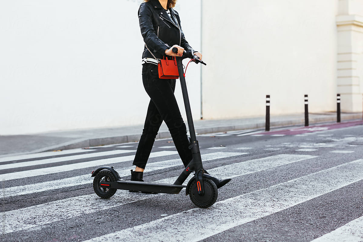 Crop woman with electric scooter walking on crosswalk