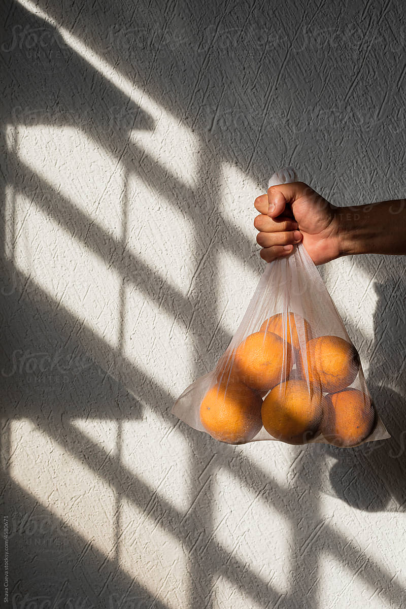 Oranges in a white recyclable mesh bag held by a male hand